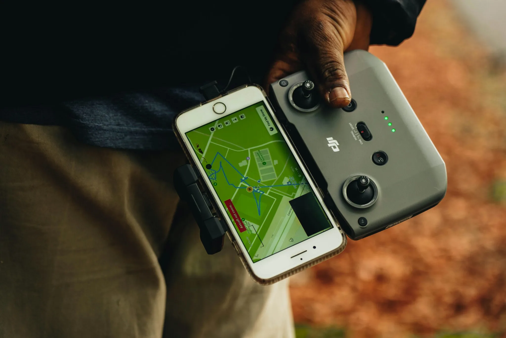 pexels-photo-13124396-13124396 Close-up of a person holding a DJI drone controller connected to a smartphone displaying a map.