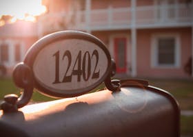 A vintage-style mailbox with the morning sun illuminating a house in the background.
